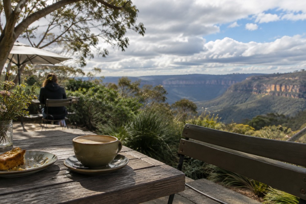 A countryside cafe table overlooking green valleys and sandstone cliffs in the Blue Mountains