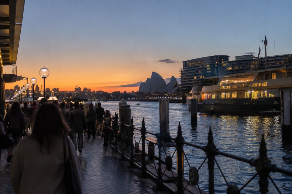 Crowded harbour foreshore walk at dusk with city lights reflecting on the water