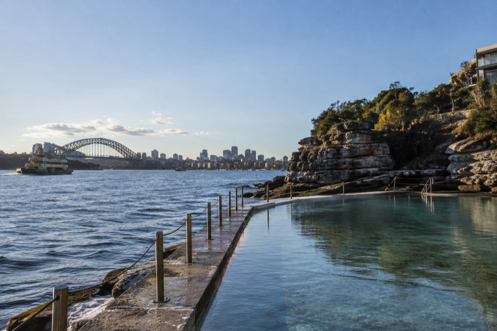 A calm Sydney ocean pool at the base of a rocky headland in early morning light