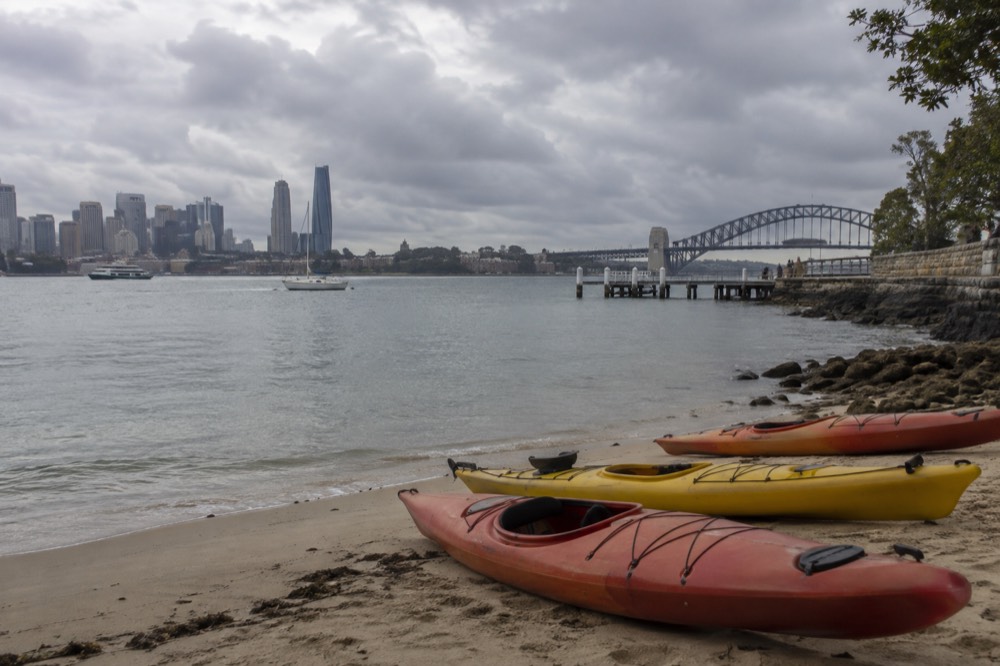 Kayaks resting on a calm Sydney Harbour beach with the city skyline across the water