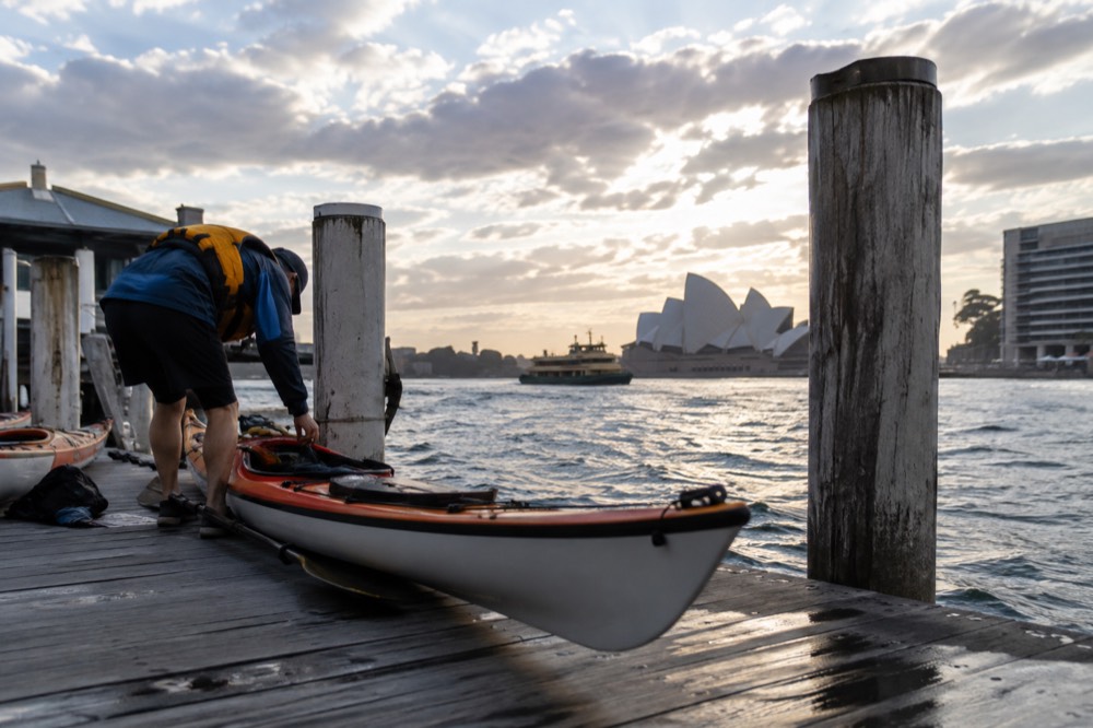 A paddler in a lifejacket checking a kayak on a wooden jetty in early light