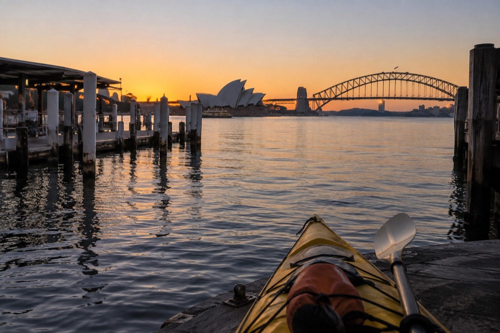 Sunrise light on calm harbour water with a dry bag and paddle resting in a kayak