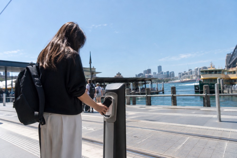 A traveller paying with a phone at a contactless reader on a Sydney light rail stop