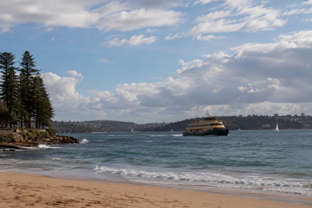 A green-and-yellow Sydney ferry approaching Manly wharf across open water