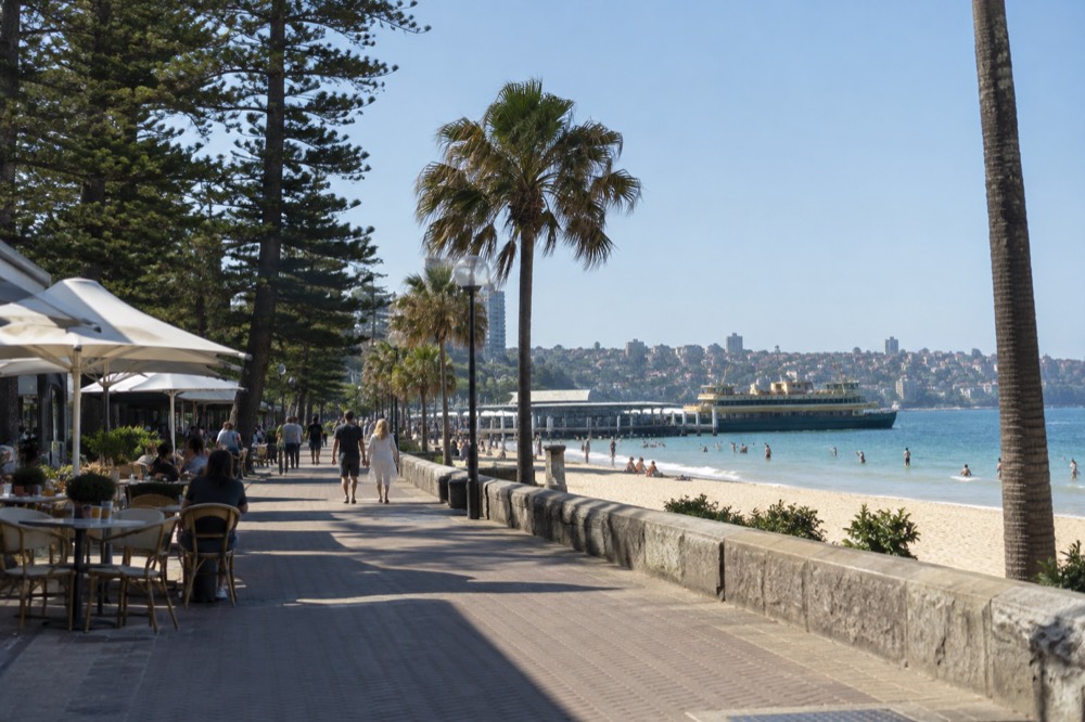 Ferry terminal and waterfront promenade with outdoor tables and palm trees