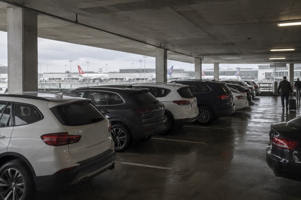 Rows of parked cars inside a covered airport car park near a terminal entrance