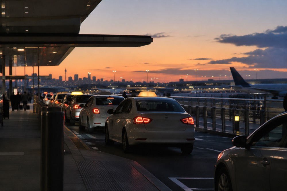 Taxis queued at a rank outside an airport terminal at dusk