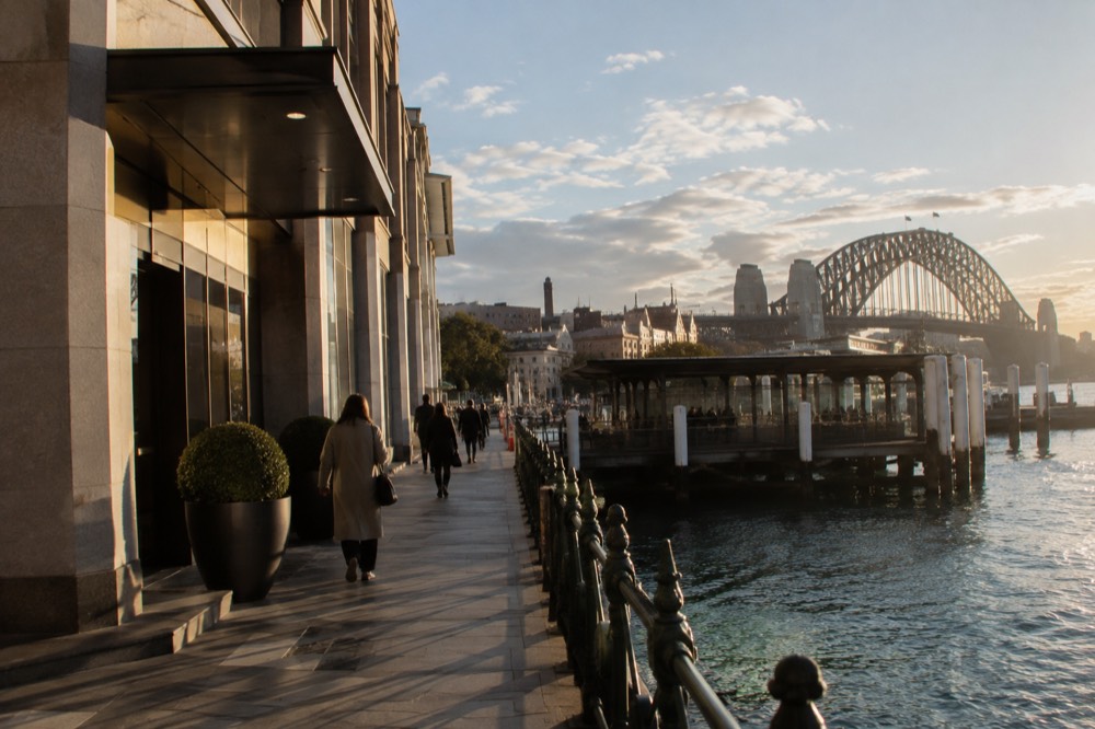A hotel entrance on a Sydney city street with the harbour bridge visible above the rooftops