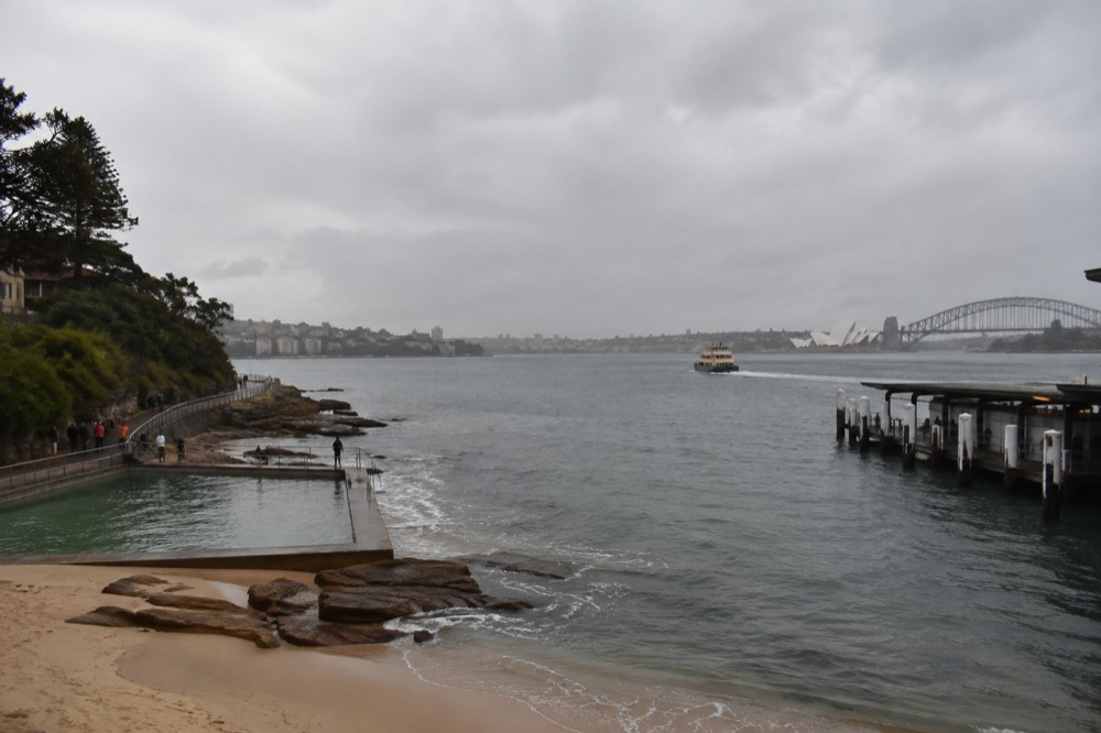 Ocean pool and sandy beach with coastal walkway curving along sandstone headland