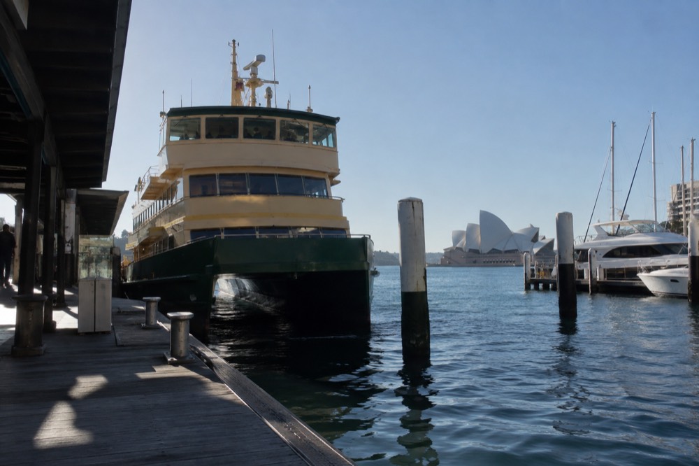 Green-and-yellow ferry at a city wharf with moored yachts behind