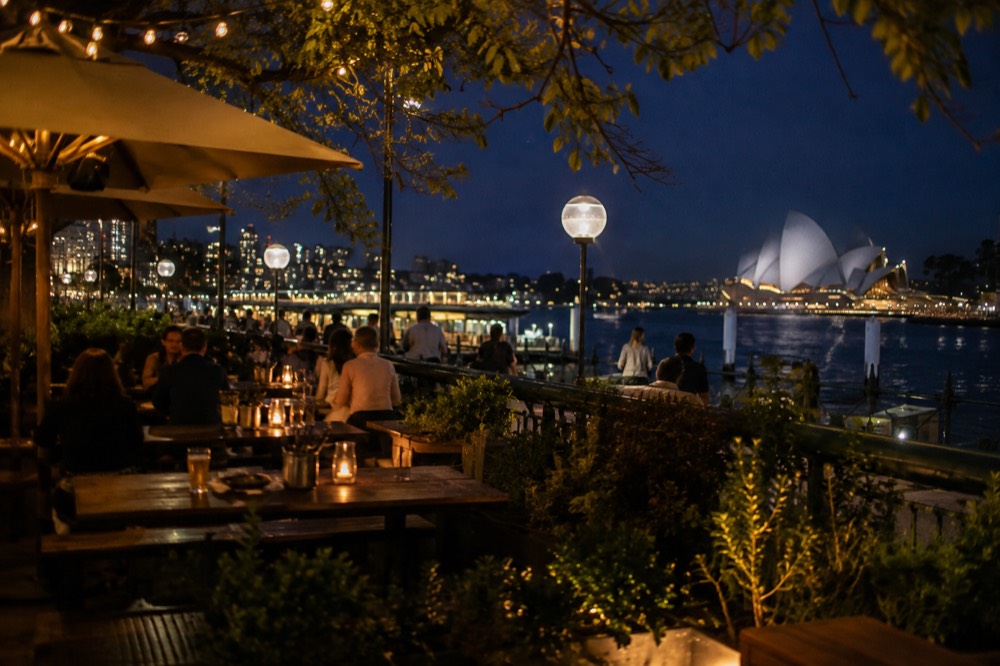 A pub beer garden with long timber tables, string lights and greenery in the early evening