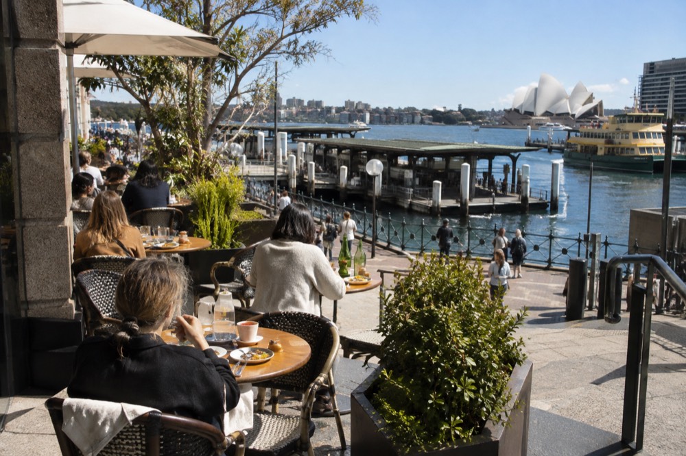 Sunlit café tables on a Sydney street corner with coffee cups and plates of brunch food