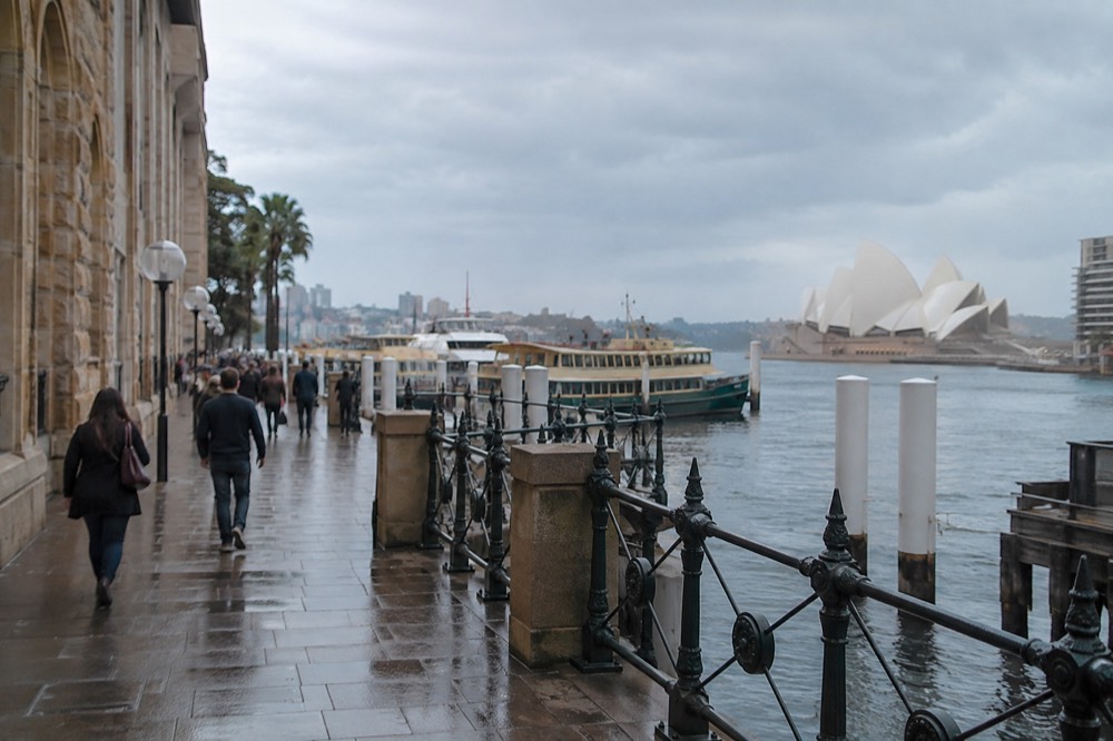 A harbour foreshore path with historic stone buildings and moored boats beyond