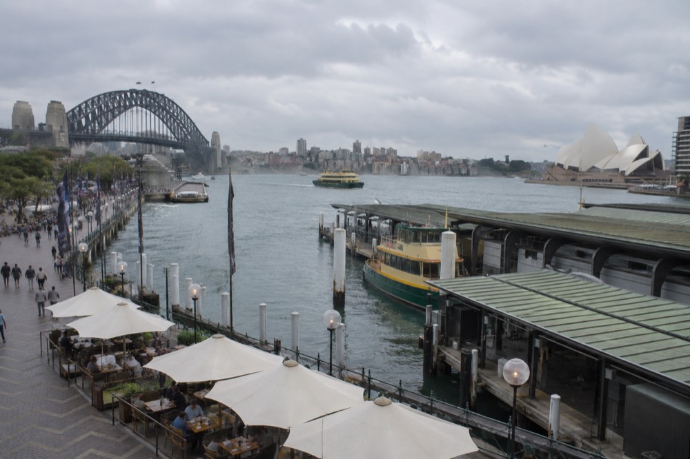 People at outdoor café tables under umbrellas on a mild Sydney afternoon