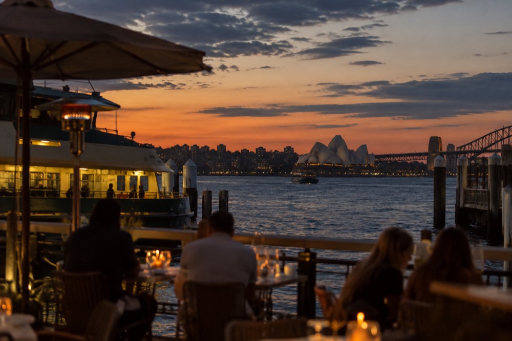 A harbour view from a waterfront dining deck at dusk with city lights