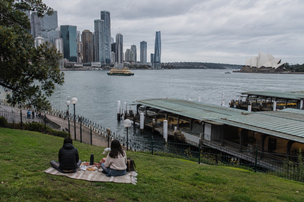 A couple's picnic spread on harbourfront grass with the Sydney skyline behind
