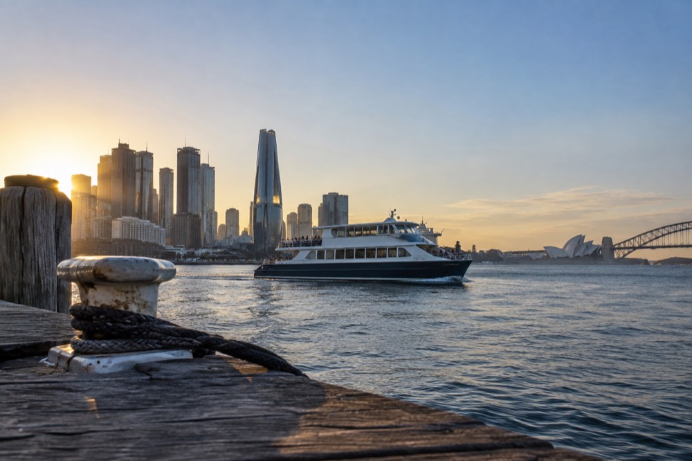 A small cruise boat crossing Sydney Harbour with the city skyline behind it in late afternoon light