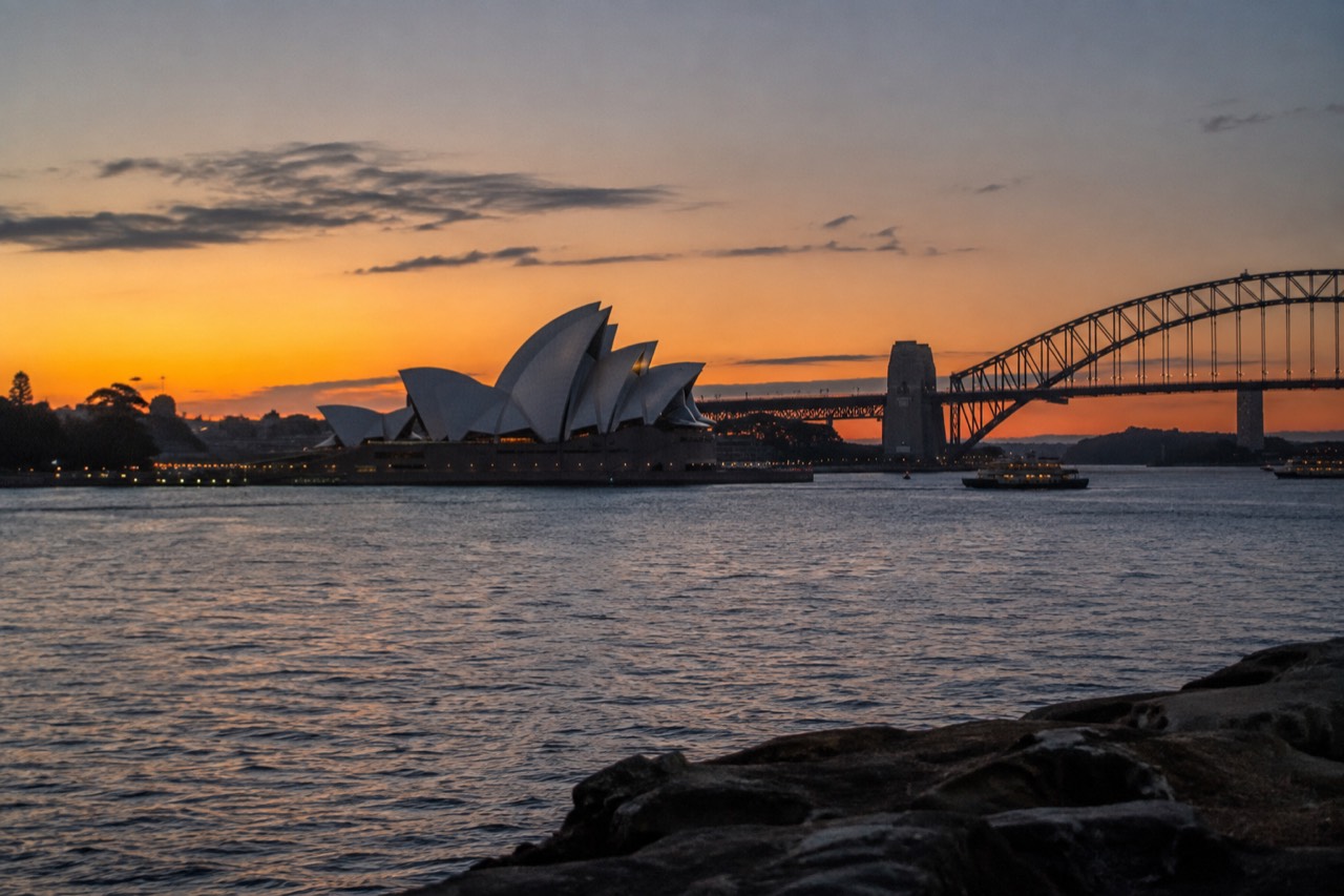 Sydney Opera House sails seen across the water at sunset with the Harbour Bridge in the background