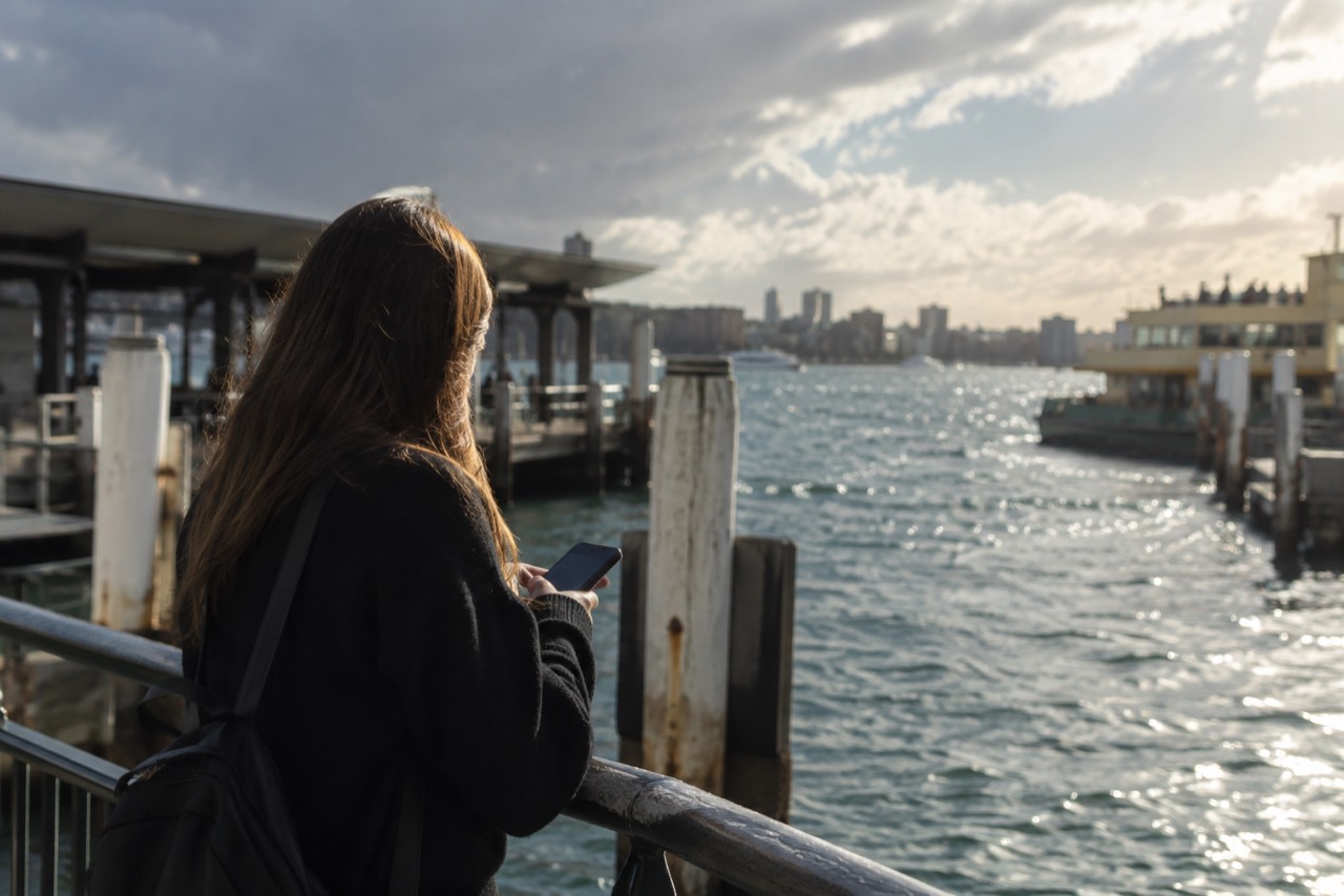 A visitor checking a phone map against the Sydney skyline across the harbour