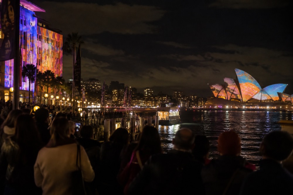Crowds watching colourful light projections on buildings around Circular Quay at night