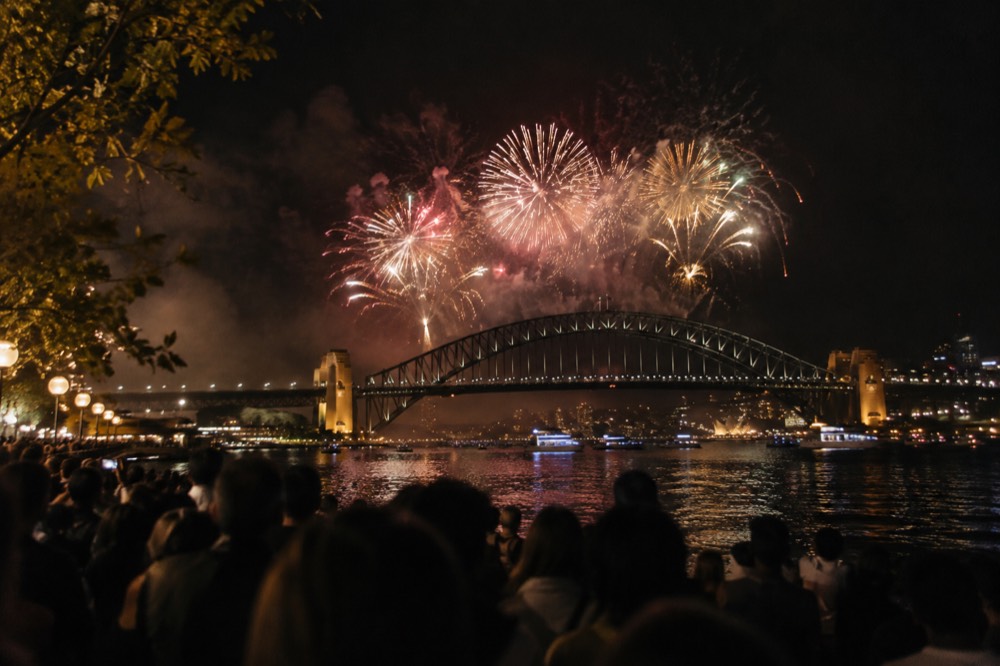 Fireworks bursting above the Sydney Harbour Bridge with crowds along the quay in the foreground