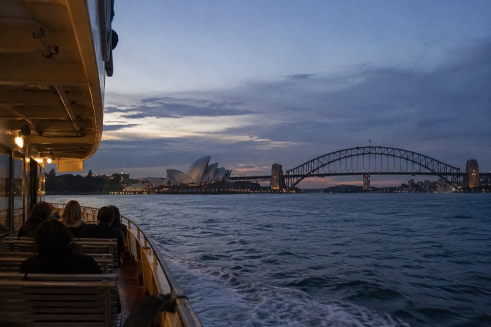 A ferry crossing Sydney Harbour at dusk with the Opera House and bridge in the background