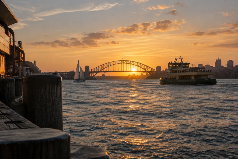 A sailing boat and a ferry on Sydney Harbour at sunset with the bridge in silhouette