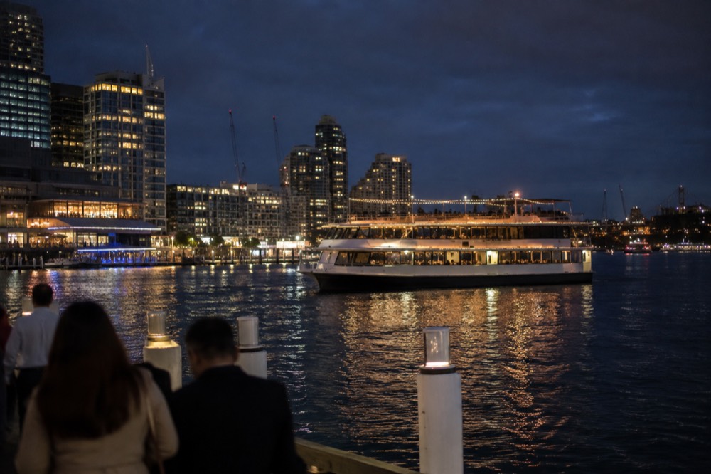 A dinner cruise boat lit up at dusk on Darling Harbour