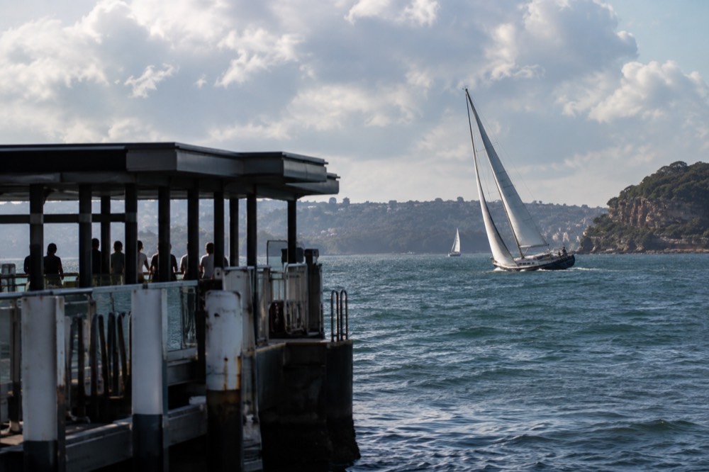 A sailing yacht heeling on open water past a Sydney headland