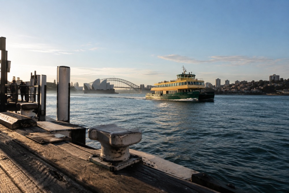 A green and yellow Sydney ferry crossing the harbour toward Manly