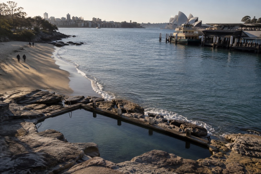 Ocean pool carved into sandstone rocks beside a calm beach at dawn