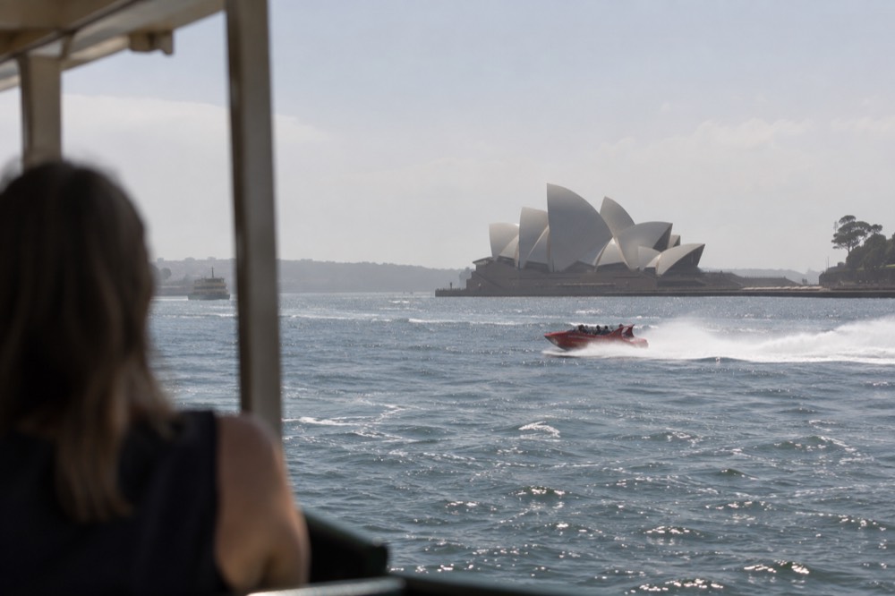 A jet boat at speed on Sydney Harbour passing the Sydney Opera House sails