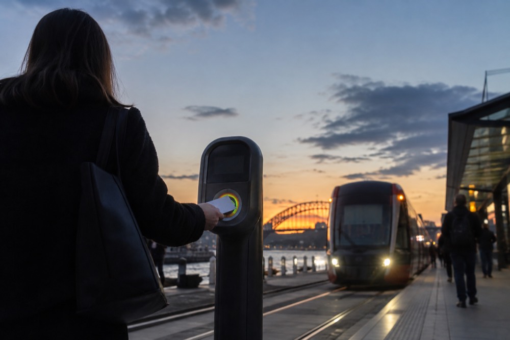 A passenger tapping a contactless card on an Opal reader at a light rail stop