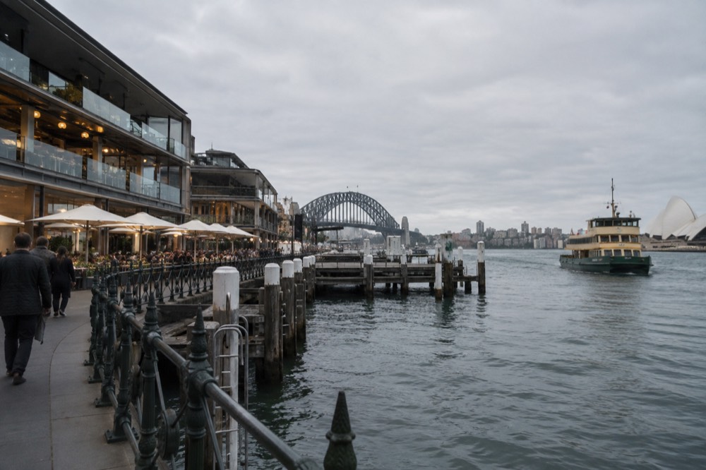 A modern waterfront market building with diners at tables along the water