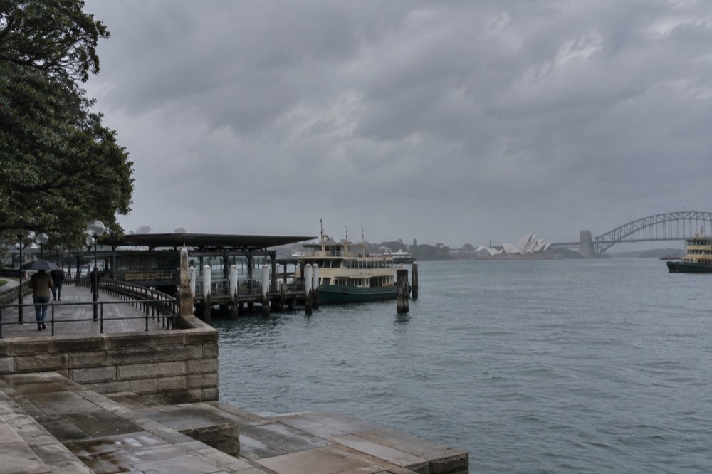 Sandstone terraced parkland meeting harbour water with moored boats