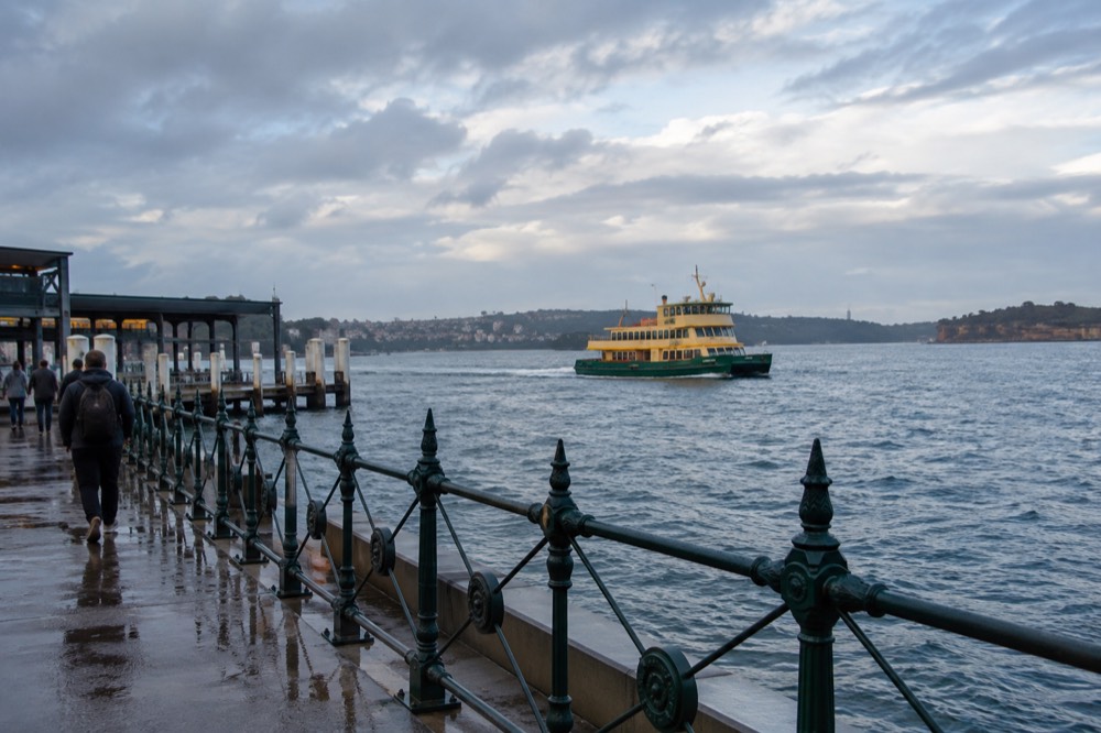 A green and yellow ferry crossing open harbour water toward a headland