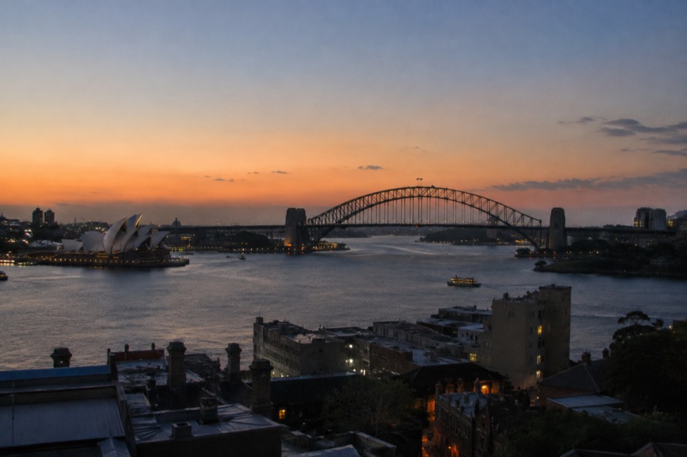 Sydney Opera House and harbour bridge seen from a high rooftop at golden hour