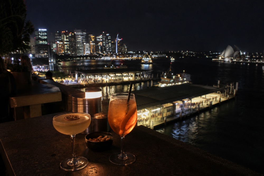 Cocktail glasses on a rooftop bar counter with the city skyline lit up behind