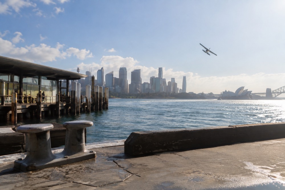 Small aircraft banking over a bright harbour with the city skyline catching morning light