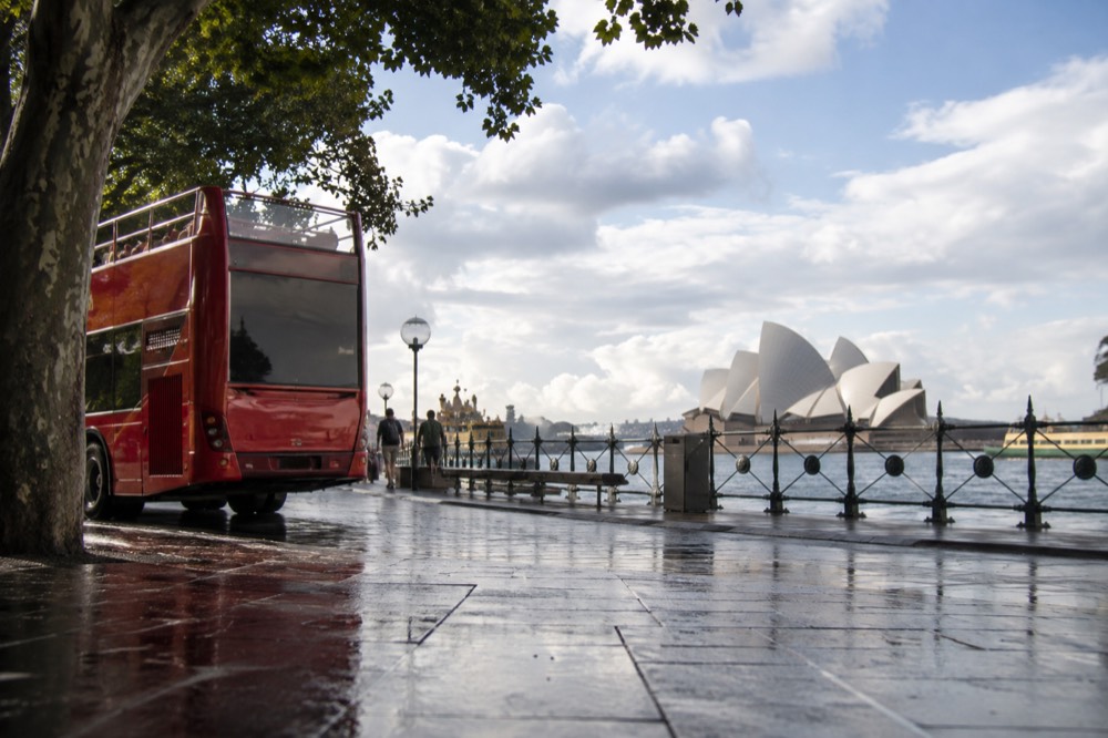 Open-top sightseeing bus parked near Circular Quay with the Opera House in the background