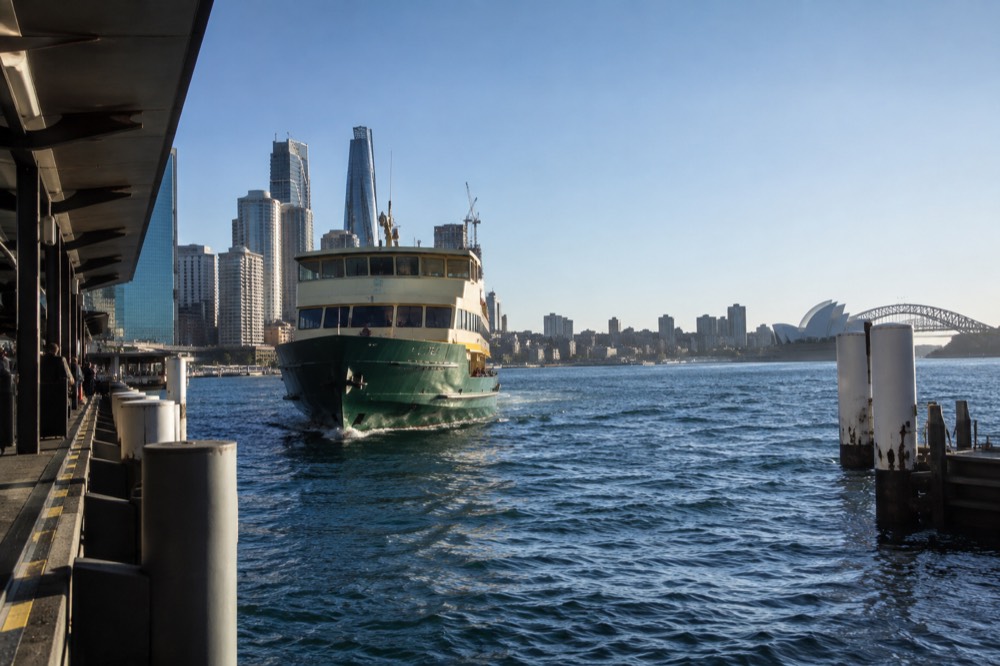 Ferry approaching a harbour wharf with city towers behind under a clear sky