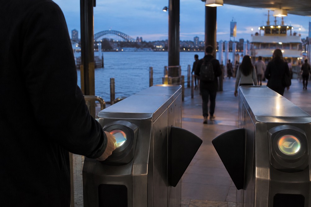 A passenger tapping a contactless credit card on an Opal reader at a train station gate