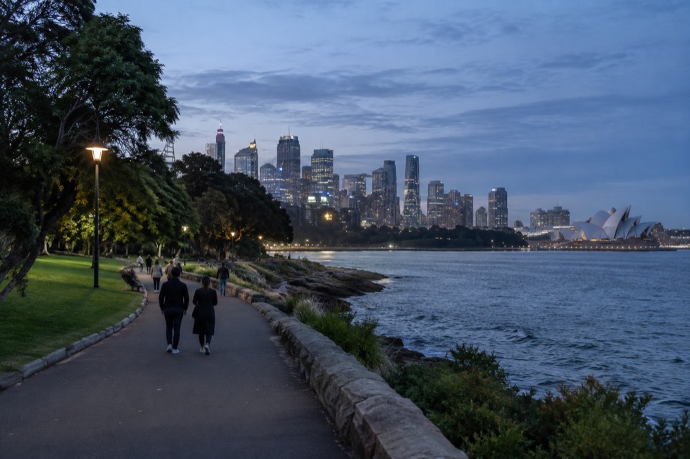A wide harbourside path through the Royal Botanic Garden with the skyline behind