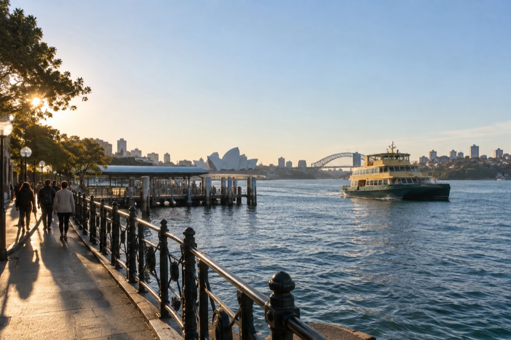 A ferry crossing the harbour towards Manly with walkers on a foreshore path