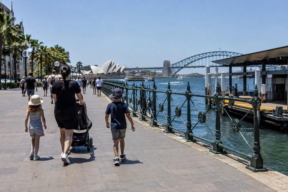 A wide paved foreshore path with a stroller and children walking beside the harbour