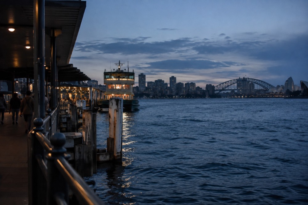 Illuminated city skyline and harbour bridge reflected in dark water at night