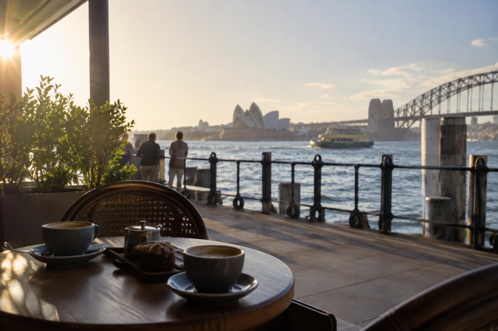 A cafe table beside a harbour wharf with coffee cups and a small tray