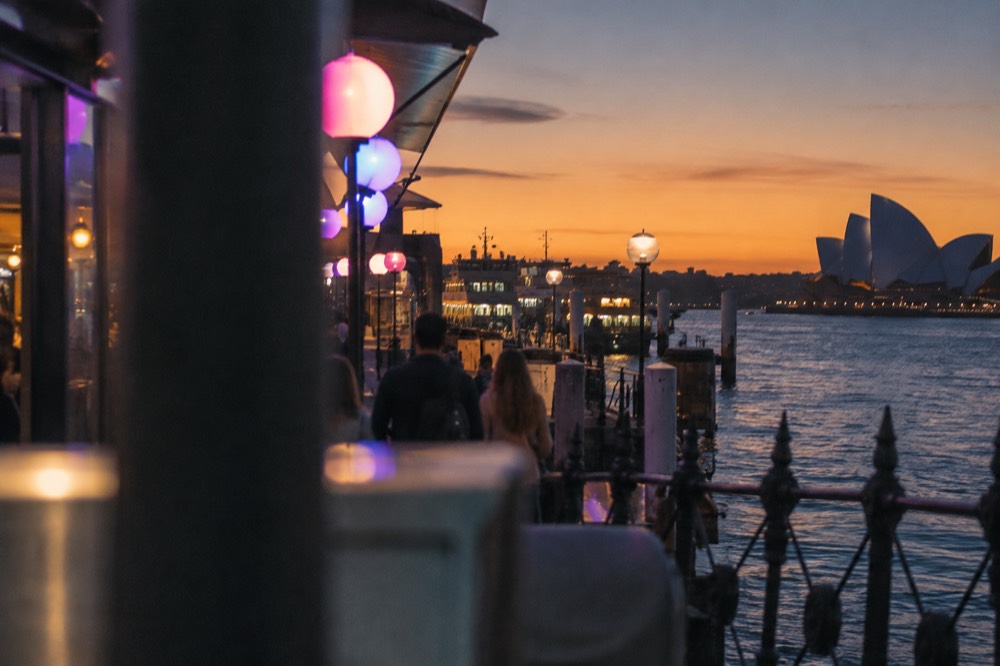 Colourful light installation glowing above a night-time promenade beside Sydney Harbour