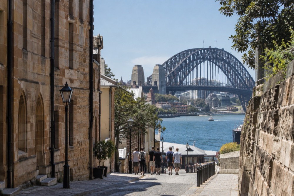 Historic sandstone buildings and cobbled lane in The Rocks with the harbour bridge overhead