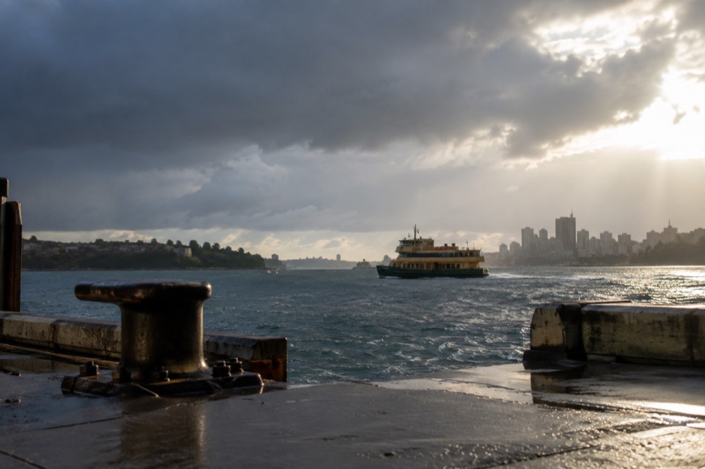 Rain clouds over Sydney Harbour with a ferry crossing between headlands